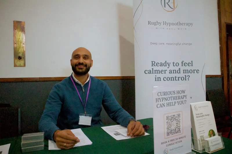 Adel Moin seated at the Rugby Hypnotherapy event stand with his banner and information leaflets