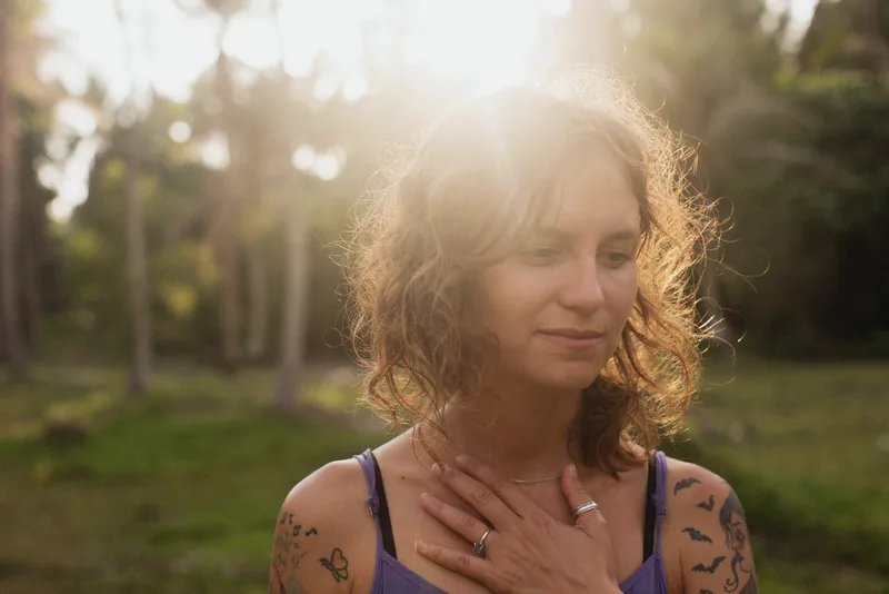 A woman outdoors with her eyes closed and a hand resting on her chest