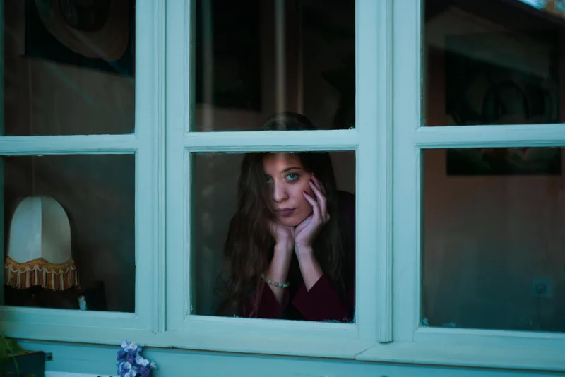 A woman looking out through a window with her hand against her cheek