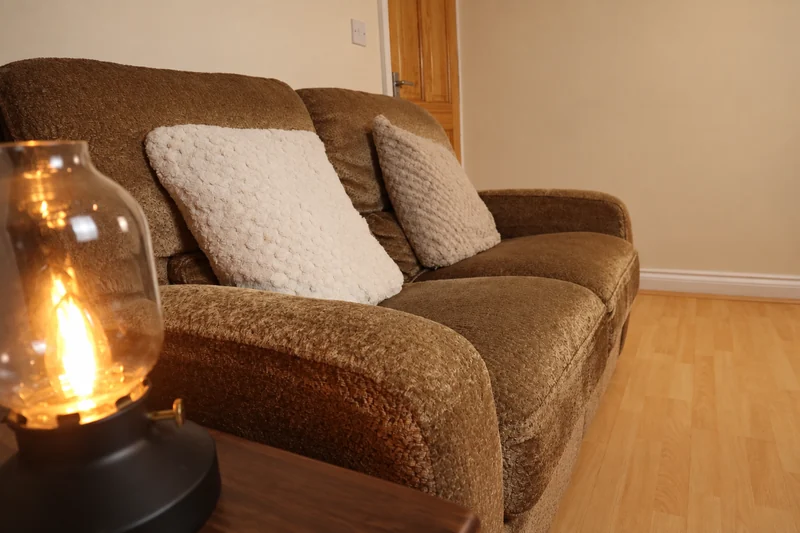 A glowing glass lamp on a table beside the sofa and cream cushions in the Rugby Hypnotherapy session room
