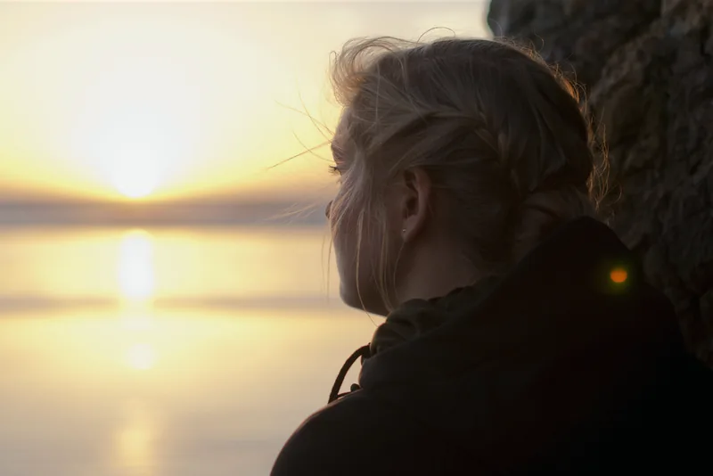 A woman looking across the water at sunset