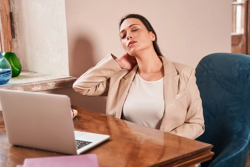 A woman at a laptop resting a hand against the back of her neck