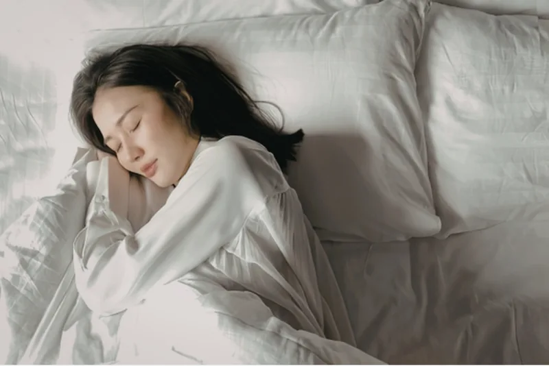 A woman sleeping on her side in white bedding