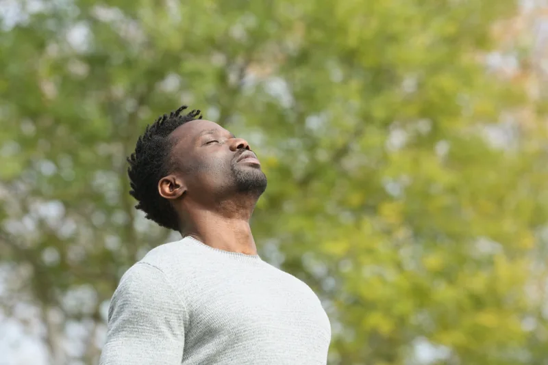 A man outdoors with his eyes closed and his face turned towards the light