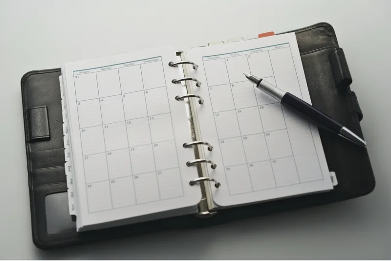 An open ring-bound calendar with a pen resting on the page
